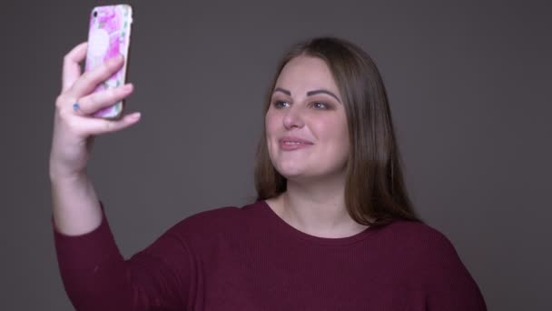 Closeup portarit of young overweight caucasian female having a video call on the phone with background isolated on gray — Stock Video