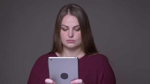 Nahaufnahme Portarit der jungen übergewichtigen kaukasischen Frau beim Surfen auf dem Tablet mit Hintergrund isoliert auf grau — Stockvideo