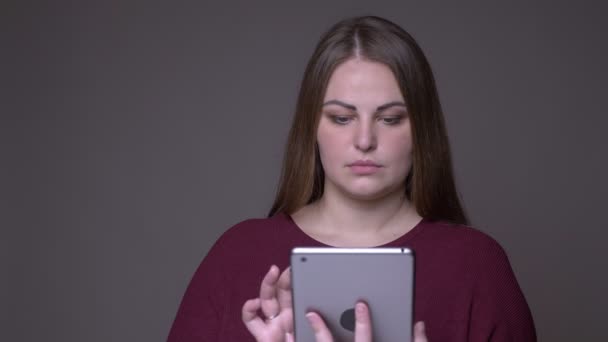 Zbliżenie portarit młodego nadwagą kaukaski kobieta za pomocą tabletu i pokazując zielony ekran do aparatu z tłem na białym tle na szarym — Wideo stockowe