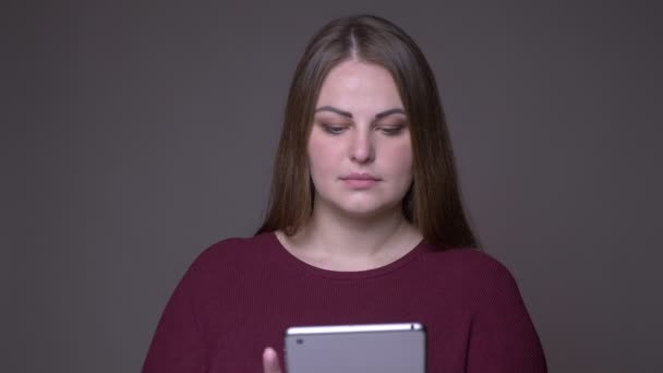 Close-up portarit van jonge overgewicht blanke vrouw met behulp van de Tablet en het tonen van groene Chroma scherm naar camera met achtergrond geïsoleerd op grijs — Stockvideo