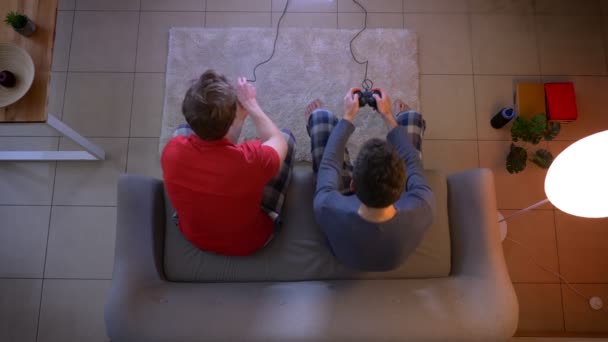 Найкращий знімок двох друзів у сплячому одязі, які грають у відеоігри за допомогою джойстика та емоційно реагують у вітальні . — стокове відео