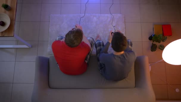 Top shot de dos amigos en pijama jugando videojuegos juntos usando joystick emocionalmente en la sala de estar . — Vídeos de Stock