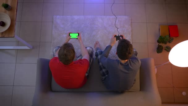 Top shot de amigos em sleepwear emocionalmente reagindo no jogo e trabalhando com smartphone na sala de estar . — Vídeo de Stock