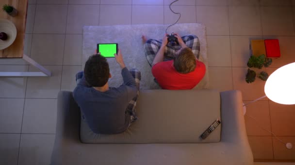 Top Shot van vrienden in nachtkleding spelen video game met joystick en Tablet in de woonkamer. — Stockvideo