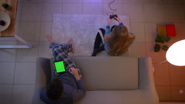 Nejlepší záběr dívky v náměsíchu hraje Videogame s pákovým ovladačem a chlapem pracujícím s tabletem v obývacím pokoji. — Stock video