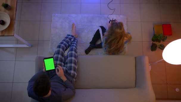 Top shot dziewczyna w bieliznę nocna gra wideo z joysticka i facet oglądania w tablecie i kiwając głową w salonie. — Wideo stockowe