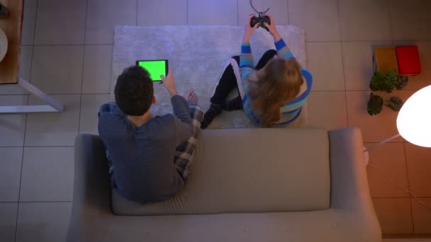 Top shot of young couple in sleepwear playing videogame with joystick and tablet in the living room. — Stock Video