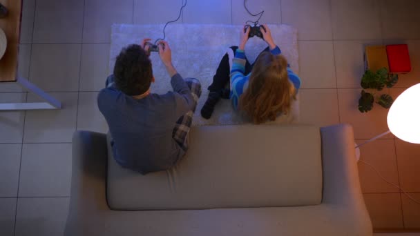 年轻夫妇在睡衣玩视频游戏与操纵杆女孩赢和家伙输在客厅的顶级镜头. — 图库视频影像
