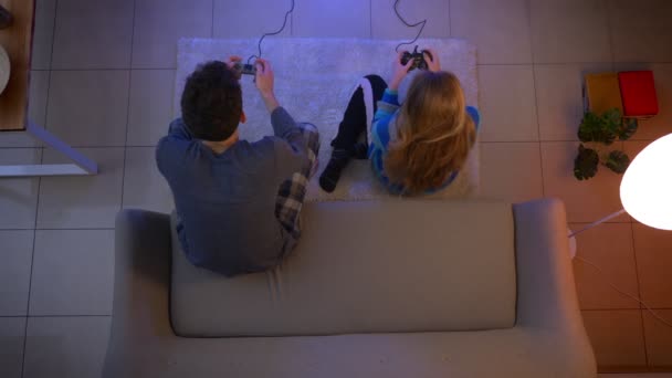 Лучший снимок молодой пары в шляпе, играющей в видеоигру с джойстиками и выигрывающей в гостиной . — стоковое видео
