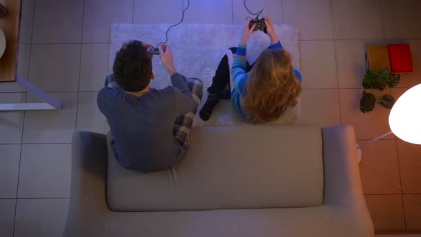 Top shot de pareja joven en ropa de dormir jugando videojuego con joysticks y ganando en la sala de estar . — Vídeo de stock