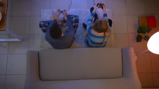 Top tiro de casal em roupas de dormir jogando videogame com joysticks no chão dá cinco felizes na sala de estar . — Vídeo de Stock