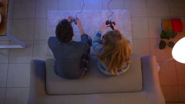 Top shot de pareja juega videojuego con joysticks molestando unos a otros pulsando los botones en la sala de estar . — Vídeos de Stock