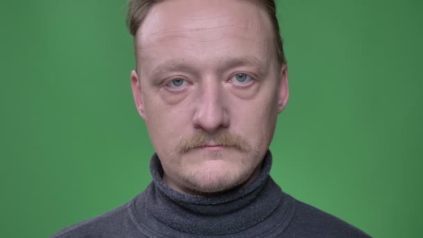 Close-up portrait of middle-aged man with beard watching into camera with no emotions on green background. — Stock Video