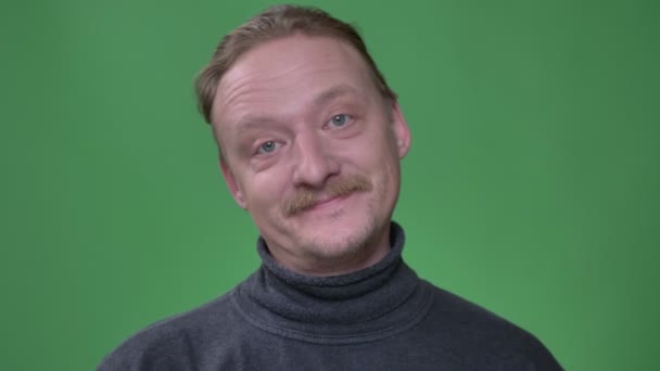 Porträtt av blond medelålders man med skägg skådning gärna i kameran Twinkles på den på grön bakgrund. — Stockvideo
