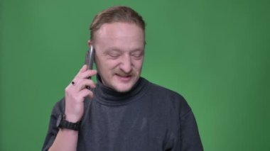 Gri pullover sarışın emekli yeşil arka plan üzerinde akıllı telefon heyecanla konuşuyor.