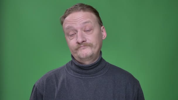 Blonďatý muž středního věku v šedém pulovníku zamyšleně obracel hlavu, aby popíral nebo nenesouhlasil na zeleném pozadí. — Stock video