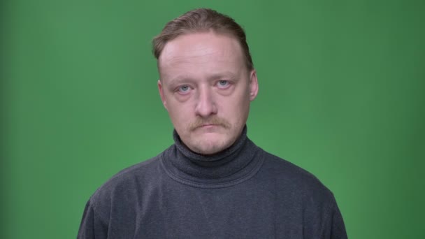Blonder Mann mittleren Alters in grauem Pullover hebt nachdenklich die Augen und blickt in die Kamera auf grünem Hintergrund. — Stockvideo