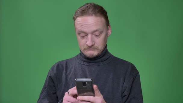 Блондинка-пенсіонер у сірому пуловері емоційно реагує на вміст смартфона на зеленому фоні . — стокове відео