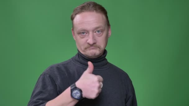 Portrait of middle-aged man with beard gesturing finger-up sign to demonstrate approvement on green background. — Stock Video