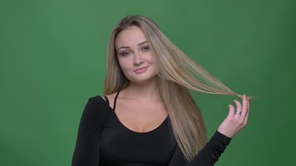 Retrato de una joven empresaria en blusa negra coqueteando con la cámara y el pelo girando alrededor del dedo en el fondo verde . — Vídeos de Stock