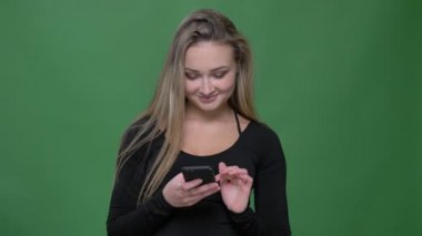 Siyah bluz genç iş kadını portresi yeşil arka planda akıllı telefon içine gülümseyerek izlerken.