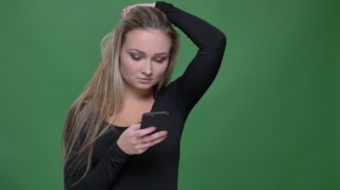 Siyah bluzgiymiş iş kadını akıllı telefona dikkat ederek bakıyor ve yeşil arka planda saç larını ayarlıyor.