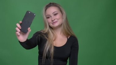 Yeşil arka planda akıllı telefonda görüntülü sohbet te neşeli konuşma siyah bluz genç model portresi.