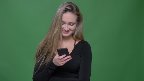 Porträtt av ung affärskvinna i svart blus titta in i smartphone och skrattretande på grön bakgrund. — Stockvideo