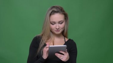 Siyah bluzlu iş kadını yeşil arka planda olumlu bir gülümseme ile tablete izliyor.