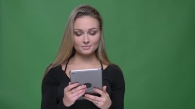 Siyah bluz konsantre iş kadını tablet dikkatle ve ciddi yeşil arka planda izlerken.