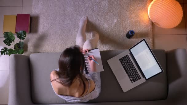 Close-up top shoot van jonge aantrekkelijke vrouwelijke studeren met behulp van de laptop zittend op de Bank in schattige sokken binnenshuis in een gezellig appartement — Stockvideo