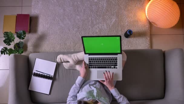 Nahaufnahme Top-Shooting der jungen attraktiven Frau mit dem Laptop mit grünem Chroma-Bildschirm sitzt auf der Couch in niedlichen Socken drinnen in einer gemütlichen Wohnung — Stockvideo