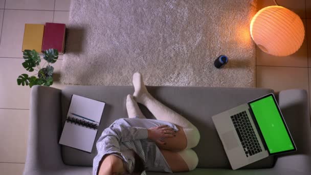 Closeup top shoot of young attractive female watching a movie on the laptop with green screen sitting on the couch in cute socks indoors in a cozy apartment — Stock Video