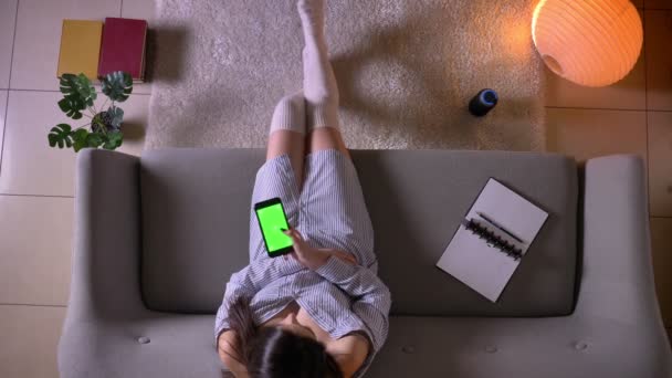 Крупный план съемки молодых привлекательных девушек-подростков, болтающих по телефону с зеленым хроматическим экраном, сидящих на диване в милых носках в уютной квартире — стоковое видео