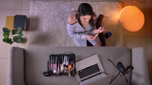 Nahaufnahme Top-Shooting der jungen attraktiven weiblichen Make-up-Artist Streaming live auf dem Laptop auf dem Boden sitzend in niedlichen Socken drinnen in einer gemütlichen Wohnung — Stockvideo