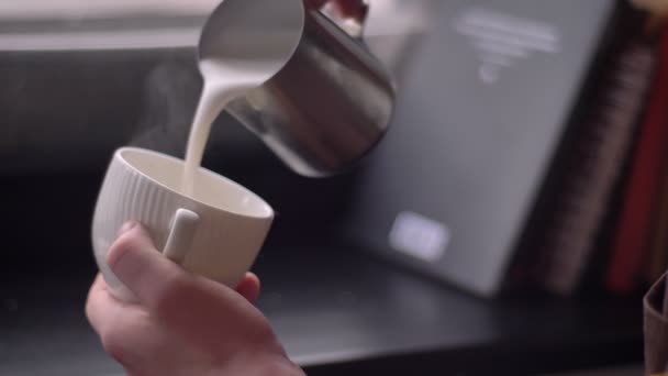 Съемки крупным планом баристы, наливающей молоко в парящий кофе в чашку с использованием серебряного кувшина в кафе в помещении — стоковое видео