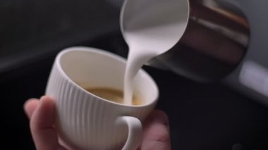Cappuccino hazırlayan gümüş sürahi kullanarak bir fincan buharlı kahve içine süt döken barista Closeup ateş