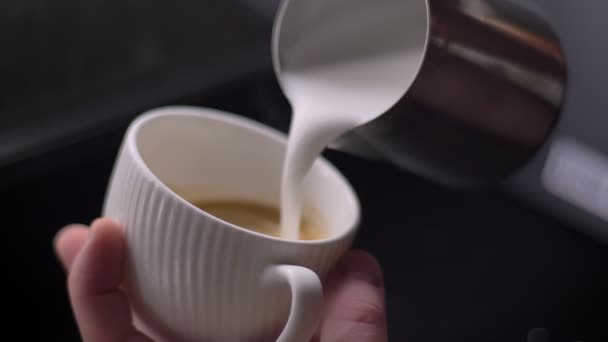 Κοντινά πλάνα του μπάρμαν που ρίχνει γάλα σε έναν ζεστό καφέ σε ένα φλιτζάνι χρησιμοποιώντας την ασημένια κανάτα για να προετοιμάσει καπουτσίνο — Αρχείο Βίντεο