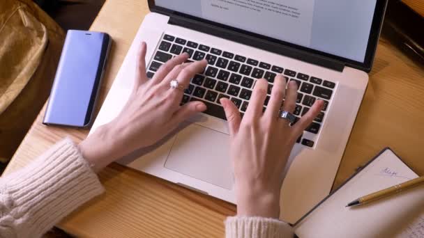 Tiro superior de close-up de mãos femininas digitando no laptop dentro de casa em uma loja de café acolhedora — Vídeo de Stock