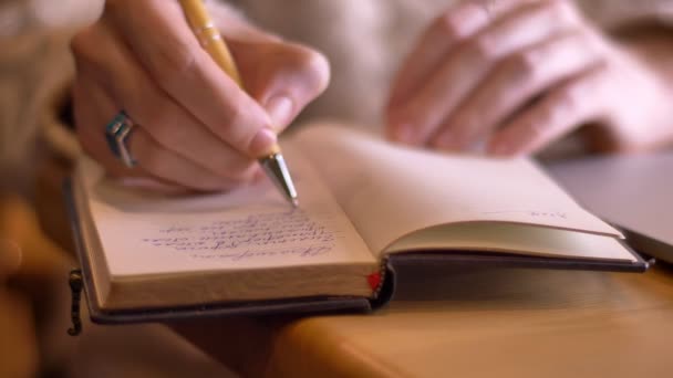 Sesión de cerca de la escritura de la mano de la mujer de negocios en un cuaderno en el interior de una acogedora cafetería — Vídeo de stock