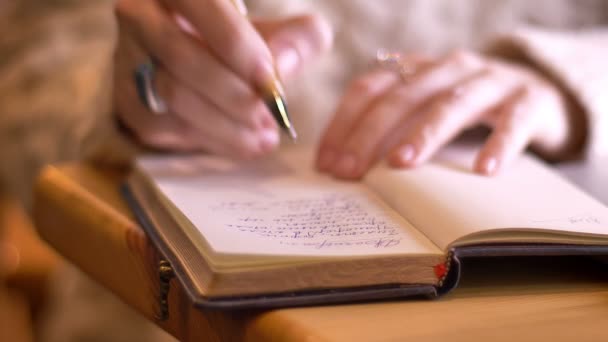 Closeup shoot of cute female teenager hand writing in a bullet journal indoors in a cozy coffee shop — Stock Video