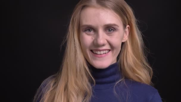 Junges blondes Model in blauem Pullover schaut mit aufrichtigem und glücklichem Lächeln in die Kamera auf schwarzem Hintergrund. — Stockvideo