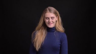 Mavi kazaklı genç sarışın model siyah arka planda kameraya sevinçle başını sallıyor..