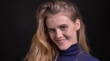 Mavi kazaklı genç sarışın manken kameraya bakıp flört ediyor ve siyah arka planda gizemli bir gülümseme takınıyor..