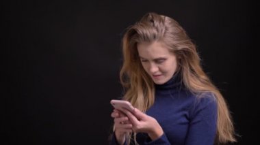 Akıllı telefonlu genç sarışın model dokunmatik ekranı sıyırıyor ve siyah arka plana odaklanıyor..