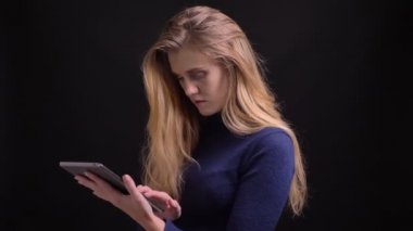 Tabletle çalışan genç sarışın model siyah arka plandaki kameraya dikkatle bakıyor..