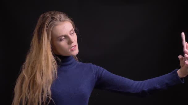 Блондинка модель робить флірт і красиві селфі-фотографії на смартфоні на чорному тлі . — стокове відео