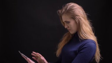 Genç sarışın model tablet üzerindeki uygulamayı açar ve yeşil ekranını siyah arka planda neşeyle kameraya gösterir.