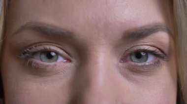 Orta yaşlı sarışın iş kadınının yakın göz portresi siyah arka planda kameraya mutlu bir şekilde bakıyor.