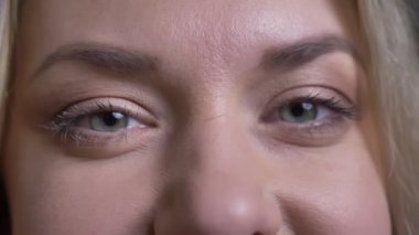 Orta yaşlı sarışın iş kadınının yakın göz portresi siyah arka plandaki kameraya hoş bir şekilde bakıyor.